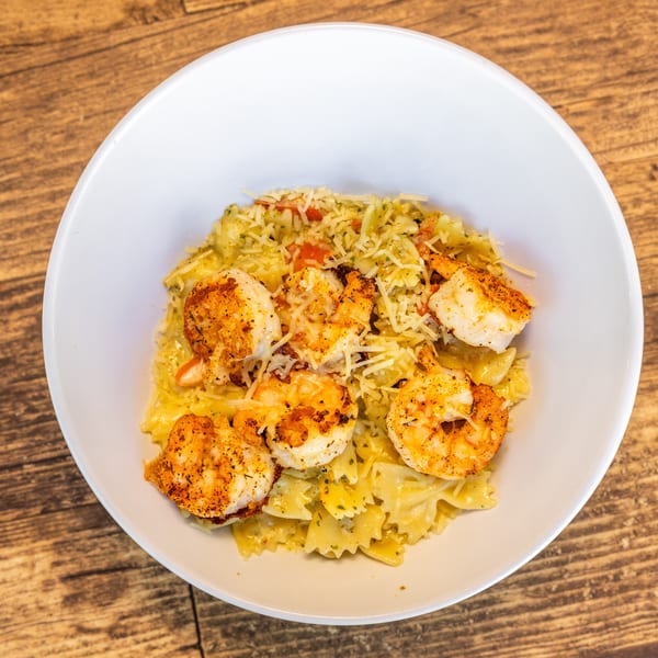 Shrimp scampi with bow-tie pasta, parmesan cheese, and diced tomatoes in a white bowl.