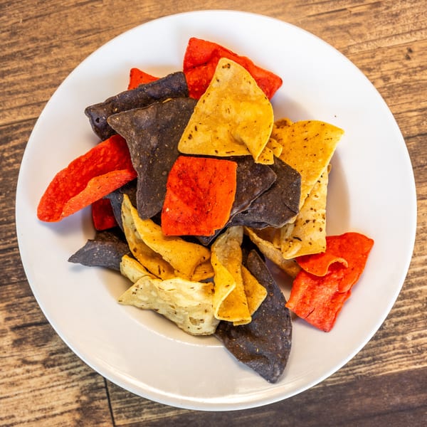 A white plate filled with red, blue, and yellow tortilla chips on a wooden table.