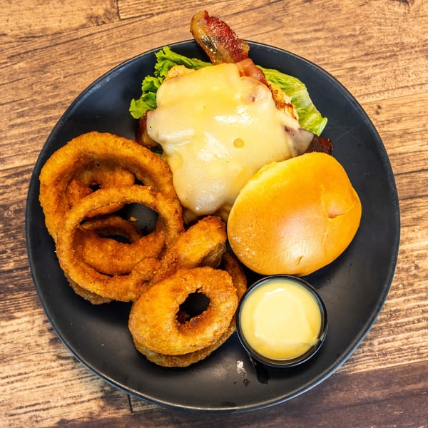 A black plate with a cheeseburger, onion rings, and a side of dipping sauce on a wooden table.