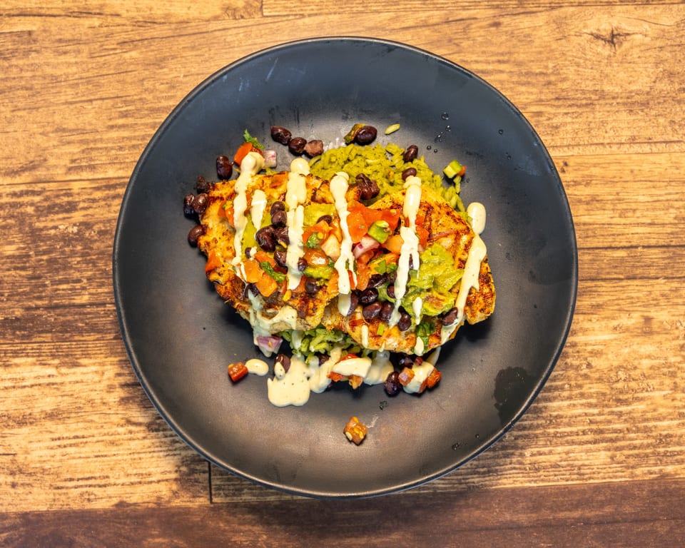Grilled chicken topped with pico de gallo, black beans, guacamole, and a creamy sauce on green rice.