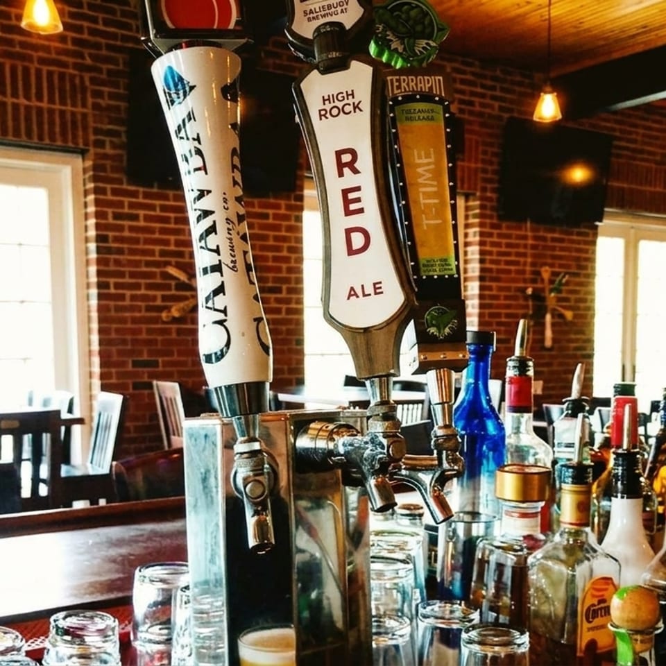Beer taps and liquor bottles on a bar counter with brick walls and sunlit windows.