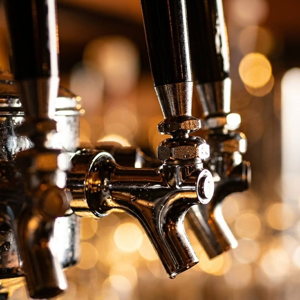 Close-up of shiny chrome beer taps with water droplets, against a warm, blurry background.