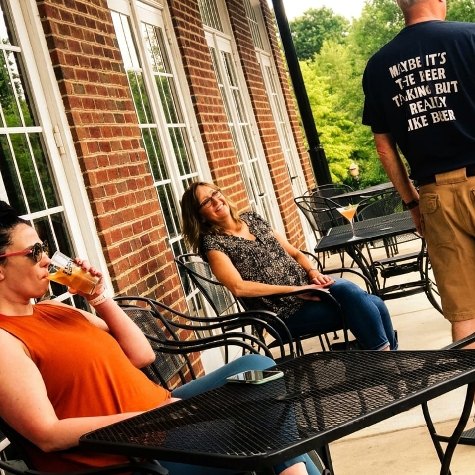 People relaxing on an outdoor patio with brick walls and large windows, enjoying drinks.